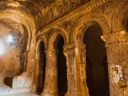 Vanhan luolakirkon sisätila Kappadokiassa, veistettyine pylväineen, kaarineen ja koristelujen jäänteineen kallioseinässä Vanhan luolakirkon sisätila Kappadokiassa, veistettyine pylväineen, kaarineen ja koristelujen jäänteineen kallioseinässä