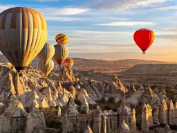 Kuumailmapalloja Kappadokian ainutlaatuisen kalliomaiseman yllä auringonnousun aikaan Kuumailmapalloja Kappadokian ainutlaatuisen kalliomaiseman yllä auringonnousun aikaan