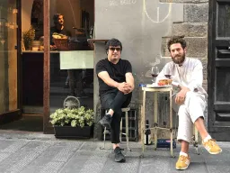 Kaksi miestä nauttii lasillisen viiniä pienessä pöydässä kadulla Kaksi miestä nauttii lasillisen viiniä pienessä pöydässä kadulla