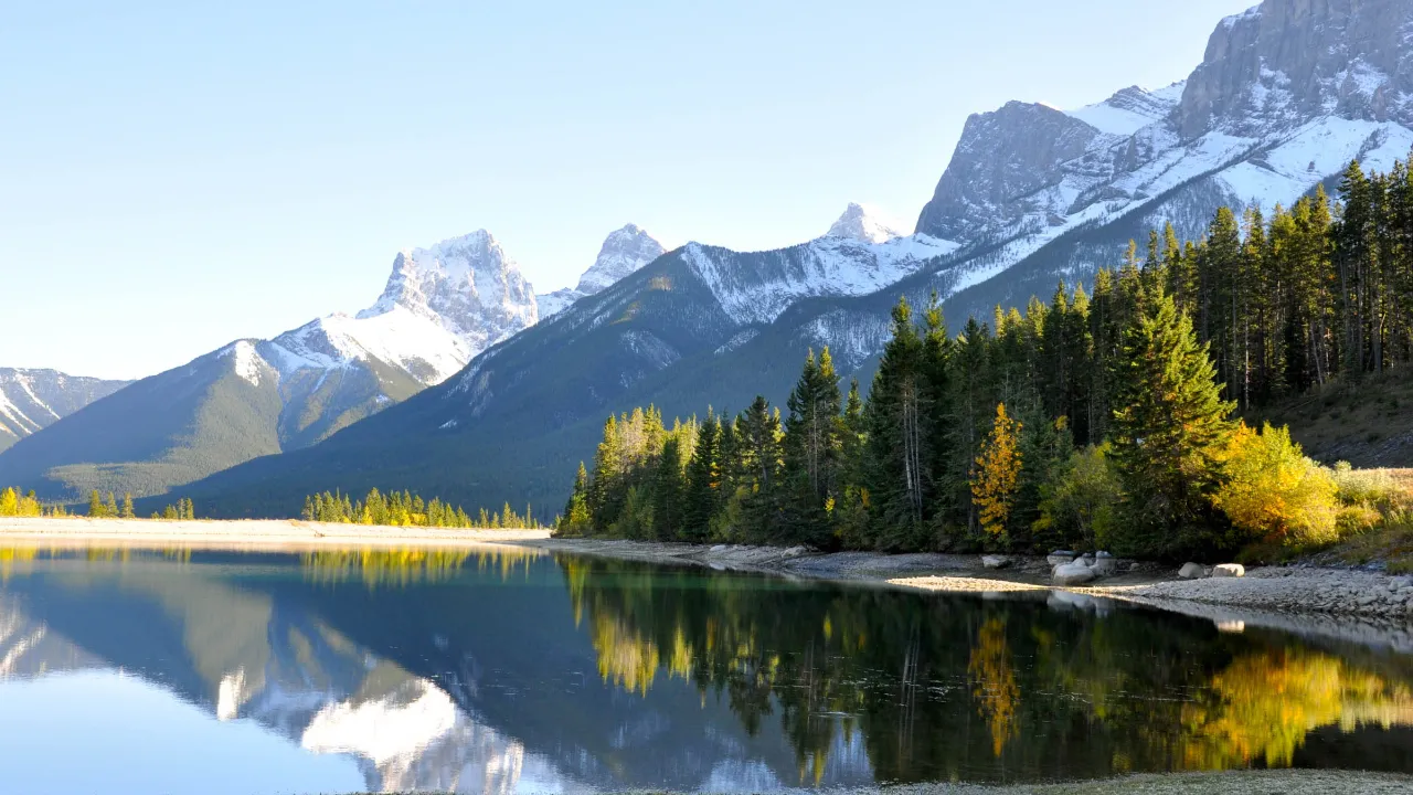 Lumiset vuoret ja metsä heijastuvat tyynessä järvessä Canmoren lähellä, Alberta